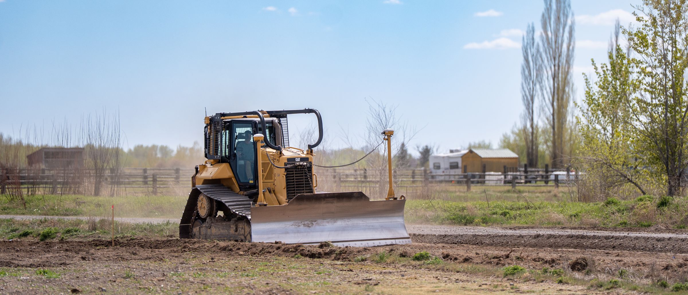 A dozer grading open ground, with poplars and a fence line behind
